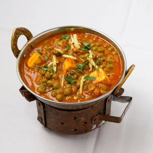 Akbar Restaurant's Matar Paneer, a vibrant Indian curry with peas and paneer cheese, garnished with ginger.