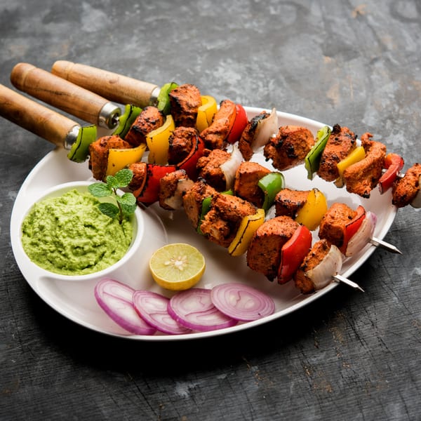 Three skewers of Indian chicken tikka with bell peppers and onions, served with green chutney and lime.