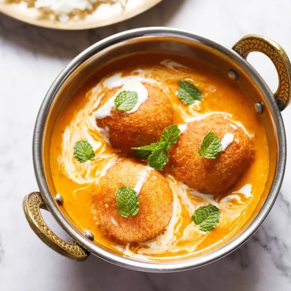 Indian Malai Kofta, fried paneer and vegetable balls in a rich orange gravy, garnished with mint.